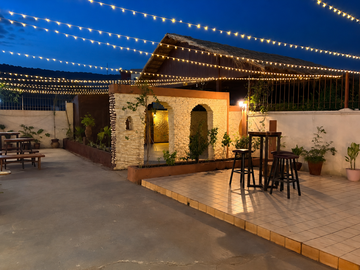 Cour extérieure de ThaoNhi illuminée avec tables hautes et jardin